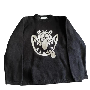 Svart stickad tröja med tecknad figur - En svart stickad tröja från KIDSON med en stor tecknad figur i vitt på framsidan. Tröjan har långa ärmar och en rund halsringning.