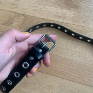 Svart bälte med silverhål från Ullared  - Svart bälte från Ullared. Bältet är i bra skick och har stor variation i storlek då det finns många hål att reglera storleken med. Finns ingen specifik storleksbestämning.