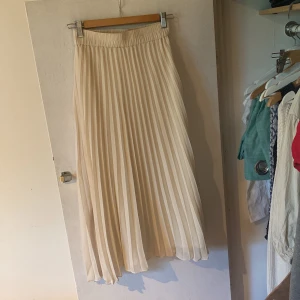Beige plisserad kjol från Monki - En elegant beige plisserad kjol från Monki. Kjolen har en elastisk midja och är i storlek XS. Den är lång och har ett flytande fall.