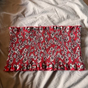 Röd tubtopp från Gina Tricot - En röd tubtopp från Gina Tricot med ett blommigt mönster i vitt och svart. Toppen har en rynkad design och volangdetaljer vid över- och nederkant. passar storlek S-L om du har stor byst 