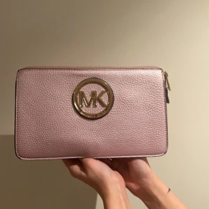 En rosa michael kors hand väska - Väskan är ganska använd men nt några större fläckar, jag har tröttnat på västan och vill därför sälja den. Vid köp så måste köparen möta mig i Stockholm på Drottninggatan 