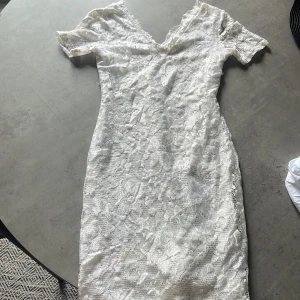 Vit spetsklänning från Club L - En elegant vit spetsklänning från Club L. Klänningen har korta ärmar och en figurnära passform. Den är tillverkad i ett spetsmaterial som ger en romantisk och sofistikerad look.