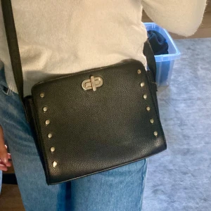 Svart axelremsväska med guldiga detaljer  - Svart liten axelremsväska med guldiga detaljer 