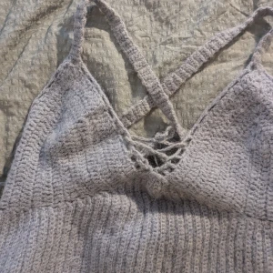 Grå stickad topp - En grå virkad topp med korsade axelband och snörning framtill. Toppen är ärmlös och har en ribbad struktur. Jag virkade den i ett lavender alpackagarn, vilket gör den lite varm. Jag tror att den hade passat på ett uterave eller sommarfest.