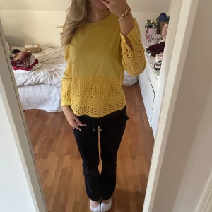 Gul blus med spetsdetaljer - En gul blus med långa ärmar och spetsdetaljer på ärmarna och nederdelen. Blusen har en lös passform och är tillverkad i ett lätt material som passar bra för vår och sommar.