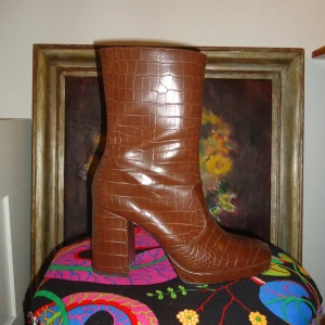 Boots strlk 40 - Högklackade boots. Brunt fejkläder. Från Monki. Små svarta fläckar på ena sidan skon (syns på andra bilden), annars väldigt bra skick. Strlk 40 (passar mig som har 39). Väldigt 60s. 