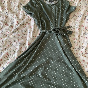 Klänning  - En grön klänning med vita prickar från Happy Holly. Använd 2 ggr. Som ny.