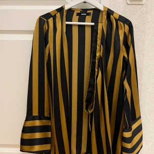Lång skojorta  - Säljer en helt ny lång skjorta från BikBok i storlek S. Skjortan är guld och svart färgad i satin material. Säljs för 50kr. Kan fraktas.