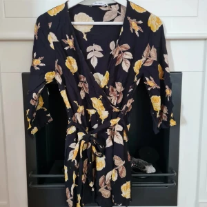 NA-KD kort blommig jumpsuit strl XS - Strl XS Snygg jumpsuit med långa ärmar och korta ben. Från NA-KD. Liten slitning på en blomma fram, litet sömsläpp på ena axeln. På knytbandet finns några märkliga streck som jag inte vet vad det är. Inget som stör.