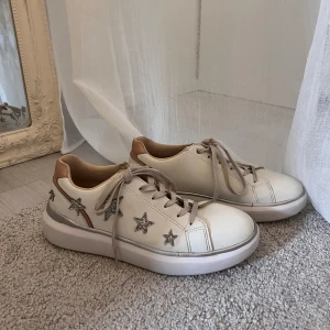 Sneakers med stjärnor  - Snygga vita sneakers med detaljer av silvriga glittriga stjärnor! Har fina ljusrosa små detaljer i bak av skon. Passar perfekt nu till vår och sommar outfits