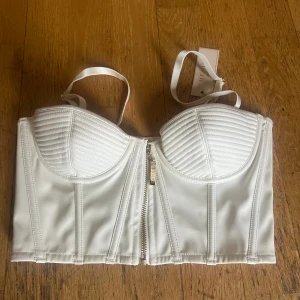 Vit bustier top från Meshki  - Läderimitation  Australiensk st 6 (XS/XXS eller 32)   Passar för A-kupa (omkrets 65 eller 70)   Säljer då den var för liten. Säljer även i större storlek (se tidigare inlägg) Originalpris 1200 SEK   Köpare betalar frakt 