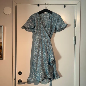 Blå omlottklänning - En blå omlottklänning med blommor, söt och somrig. I princip nyskick pga för liten från inköp, använt fåtal gånger. Pris kan diskuteras