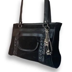 Axelväska  - En väska i fint skick, som går ner till midjan när man bär den runt axeln. Dödskallekedjan ingår! Vet ej märke. MÅTT: Höjd 21cm, bredd 28cm & djup 8-11cm  MGF L1