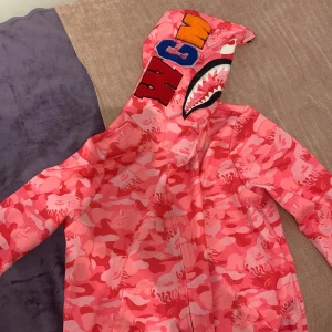 Rosa bape zip up hoodie - Rosa bape zip up hoodie med zip ända upp till luvan, 3D bokstäver på luvan. Storlek s-xs unisex. Aldrig använd!