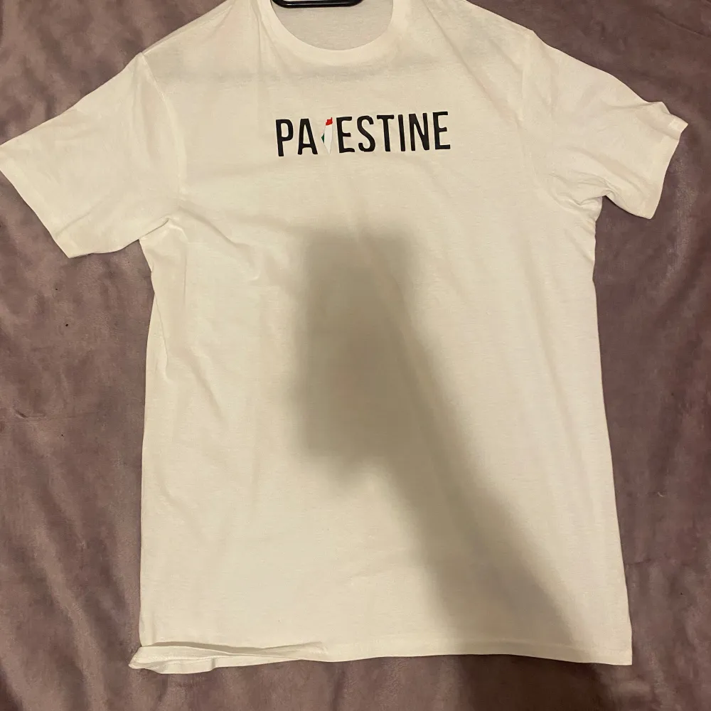 Vit t-shirt med text som säger ” PALESTINA”. T-shirts.