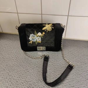 Svart axelbandsväska  - Svart axelbandsväska med tryck  Aldrig använd, bara stått i en hylla Ett dragkedjefack på insidan plus ett utan dragkedja 