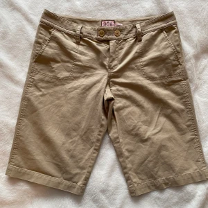 Beiga chinosshorts från Juicy Couture i strl 8 (38) - Beiga chinosshorts från Juicy Couture i strl 8 (38).  Sparsamt använd och i fint begagnat skick   Mått Midjan: 43 cm Längd från grenen och ner: ca 33 cm  Bomull 