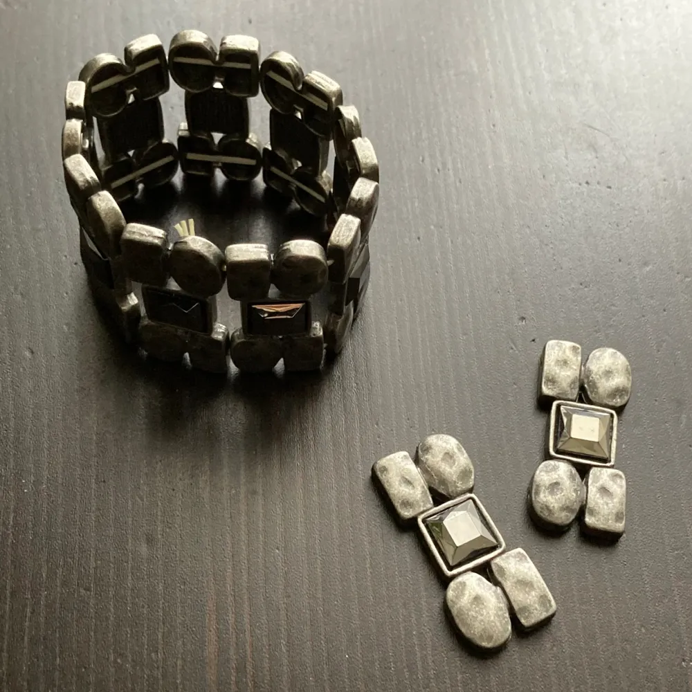 Elastiskt armband i silverfärgad metall med glansiga stenar. Har kortats av. Bredd: 3,9 cm, innerdiameter: 4,6 cm.. Asusteet.