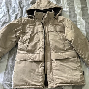 Dunjacka med regnskal - En biege dunjacka med ett polyester regnskal i storlek L. 