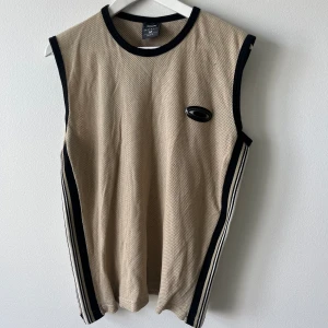 Linne från Oakley - Beiget linne från Oakley, randigt i sidorna i svart, vitt och beiget. Svalt till sommaren då det är stickat som ”nät”. Känns som bomull.    Passar både tjej och kille 💛