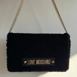 Moschino väska i svart med guldiga detaljer, som ny, inga skador! Banden kan justeras. Köparen står för frakt.