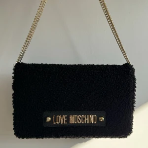 Love moschino - Moschino väska i svart med guldiga detaljer, som ny, inga skador! Banden kan justeras. Köparen står för frakt.