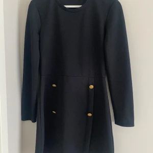 Svart klänning med gulddetaljer - Superfin! Köpt på Sellpy men själv använt den 1 gång av mig. Fint skick. Har mer att ge🥰