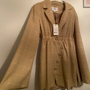 Beige/brun klänning - Beige/brun klänning från nakd, den är helt oanvänd och i väldigt bra skick! Sitter väldigt fint på! Storlek 34. Köpte den för 600kr 