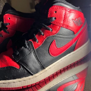 Nike Air Jordan 1 mid, röda - Storlek 38, skadad fram på skon (bild 2) , skadad i hälarna på båda skor (bild 3), creasade. Annars i bra skick! Köpta för 1 500kr 
