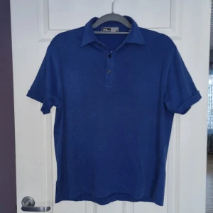 Pikétröja  - Blå pikétröja från Oscar Jacobson i storlek M. Har en sprucken sömn i nacken (se bild)