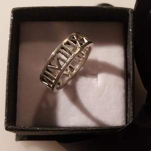 En ring i silver som visar romerska tecken runtikring. Ett stilrent tillval som bidrar till en snygg outfit. Hör av dig om funderingar uppkommer!
