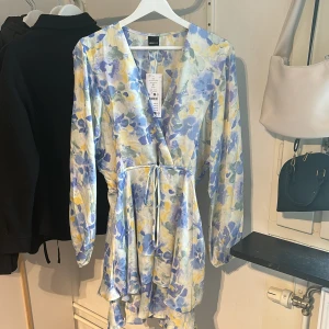 Mini drawstring dress från Ginatricot  - Blommig klänning med oversize fit. Den har en v-ringning och volanger längst ner. Klänningen är helt ny och jag köpte den för 499kr men på hemsidan kostar den nu 250 kr men är slutsåld.☀️⛱️💙