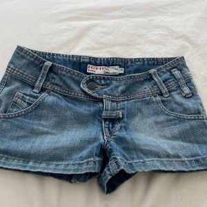 Blå jeansshorts från Ichiban - Ett par blå jeansshorts i storlek Dam Xs. Säljer eftersom de var lite för tajta på mig! Shortsen har en femficksdesign med bälteshällor och en knapp- och dragkedjestängning. De har en något sliten look med dekorativa sömmar på bakfickorna.