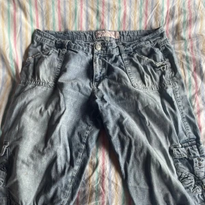 Blå jeansshorts från Staple Wish - Ett par blå jeansshorts med flera fickor och knappstängning. Shortsen har en avslappnad passform och är knälånga.