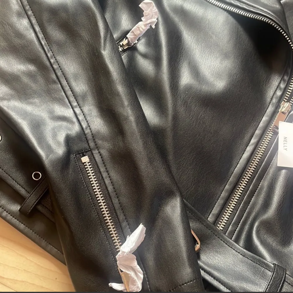 Grymt Snygg svart Biker Jacket med bälte i midjan från Nelly. Jackan har dragkedjor framtill och på fickorna. Den har även en dragkedja på varje ärm.  Jackan är oanvänd . Nypris 679kr. Jackor.