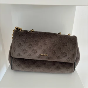 Guess handväska  - Handväska från Guess. Väskan är i sammet och fin i modellen. Är i rätt så bra skick förutom att bandet mellan kjedjan har släppt.(går att fixa enkelt)