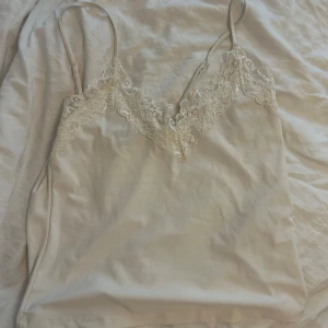 Beige linne med spetsdetaljer - Säljer ett supergulligt vitt linne med smala axelband och vackra spetsdetaljer vid halsringningen. Perfekt för sommaren eller som ett lager under en tröja. Linnet är i bra skick och väldigt bekvämt att ha på sig. Passar både till vardags och fest! inga defekter på linnet. priset kan diskuteras. 