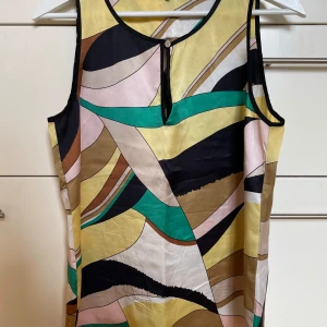 Mönstrad ärmlös topp från Marella - Säljer en snygg, ärmlös topp från Marella. Toppen är tillverkad i 100% siden och har ett abstrakt mönster i färgerna gul, grön, svart, beige, brun och rosa. Den har en knappdetalj vid halsen och är perfekt för sensommaren. Passar både till vardags och fest!