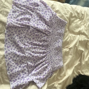 Lila blommig kjol från Gina Tricot - Säljer en superfin lila blommig kjol från Gina Tricot i storlek L pågrund av att den är alldelles för stor för mig. Den har bara använts en gång. Kjolen har en smockad midja som gör att den sitter bekvämt och snyggt. Den är perfekt för sommaren men även höstiga dagar med ett par strumpbyxor till, och har en söt volangdetalj längst ner.