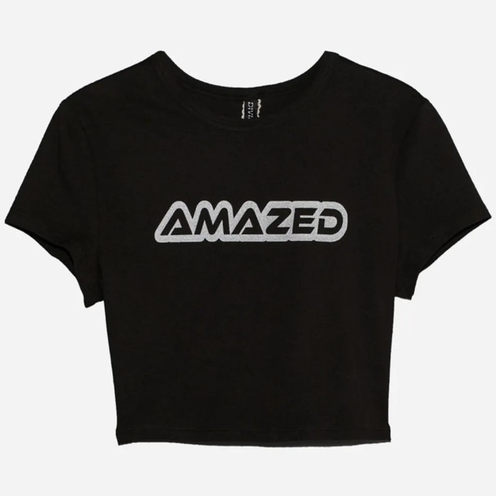 Säljer en svart croppad t-shirt med texten 'AMAZED' i silver på bröstet. T-shirten har korta ärmar och en rund halsringning. Prislapp finns kvar då den aldrig kommit till användning pga att det inte är min stil. 🖤. T-shirts.