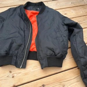 Svart bomberjacka från 157 - Säljer en svart bomberjacka från 157 i storlek XS. Jackan har en cool orange insida och en dragkedja framtill. Perfekt för höst och vår!