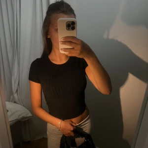 TOPP MED ÖPPEN RYGG - Säljer en snygg svart ribbad topp som är perfekt för fest eller en utekväll. Toppen har korta ärmar och en tight passform som framhäver figuren. Den är croppad och har en öppen rygg med knytband som ger en extra detalj. Materialet är mjukt och stretchigt, vilket gör den bekväm att bära.