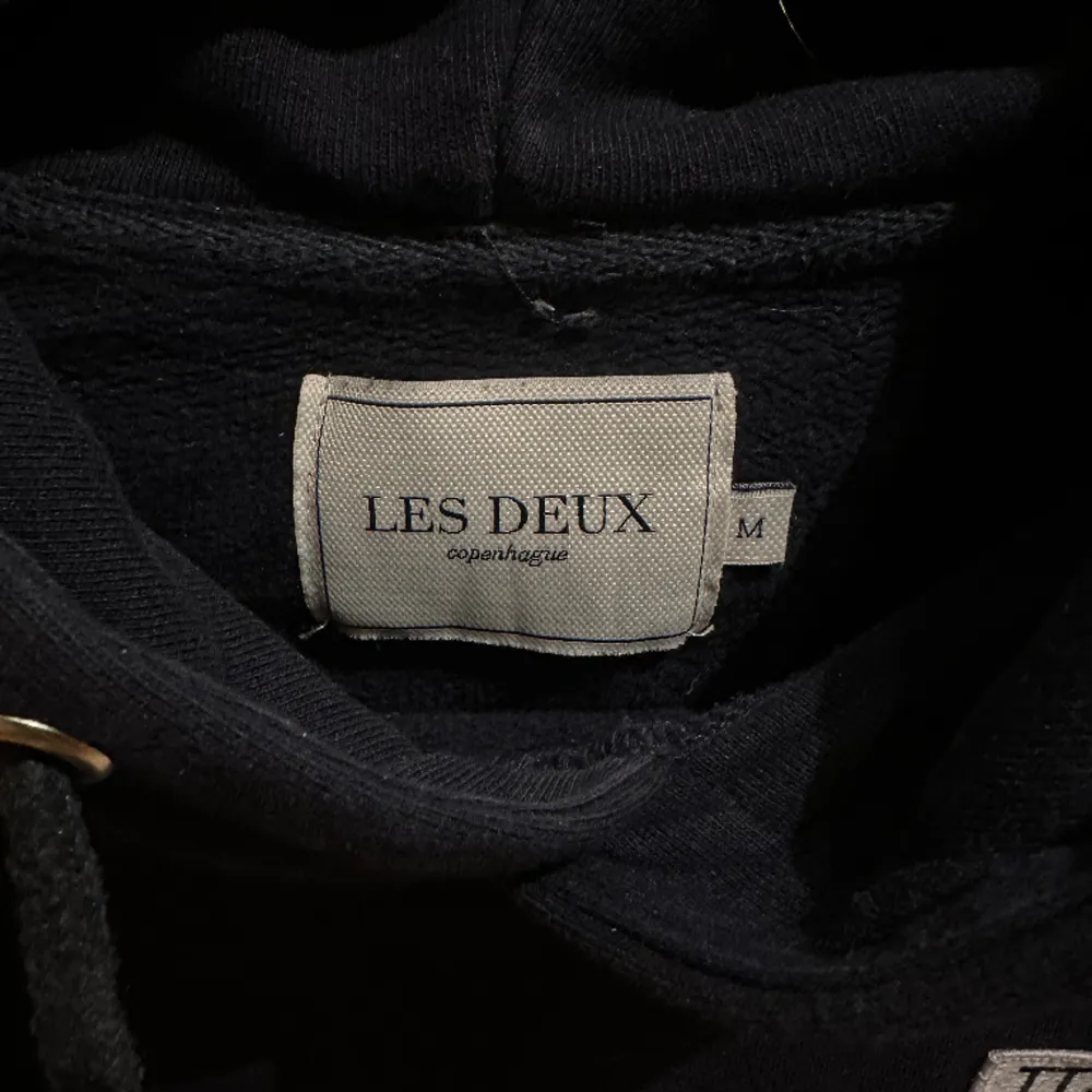 En mörkblå hoodie från Les Deux med skön passform. Nästan oanvänd och i bra skick. Den har en liten logo på bröstet som ger ett snyggt statement. Snören med silvriga ändar som tyvärr ramlat av.. Hoodies.