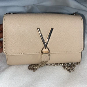 Valentino bags - Divina  - Valentino väska i färgen beige. Väskan har guld detaljer och är i jättebra skick! Den har även en guldkedja så att man kan bära den crossbody samt göra den till en axelväska. Ordinaries pris: 669kr Säljer för 380kr!
