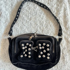 Núnoo väska - Svart Nunoo väska i mocka med silvriga detaljer. Skick enligt bild, slitningar lite här och där. Finns en fläck på undersidan som har stelnat och har inte riktigt försökt få bort den. Säljes därför billigt 🫶🏽