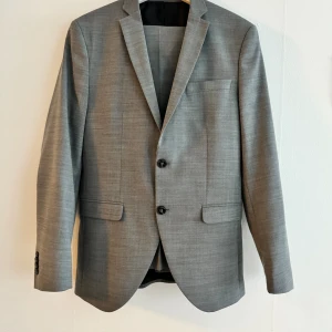 Grå kostym - Säljer en snygg grå kostym från Jack & Jones Premium, kavaj med byxor.  Premium i super slim. Kavaj i storlek 46 , byxor i storlek 44. Använd två gånger. Skickar snabbt inför din student. 