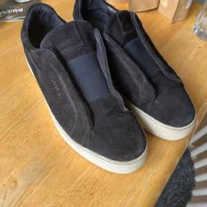 Axel arigato mocha - Schyssta skor. Köpta på NK Säljs i befintligt skick. Finns tecken på användning och ett litet hål fram på skon