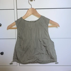 Grön parachute top från H&M  - En grön parachute top i nästan oanvänt skick! Som sagt bara använd ett fåtal gånger, så ingen risk på skador till plagget. Går att knyta vid i midjan, se bild. Köpare står för frakt, pris 30 kr.