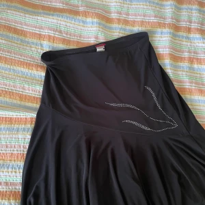 Svart klänning från Fashion One - En elegant svart kjol från Fashion One med en enkel design och dekorativa stenar på framsidan. storlek L-XL 