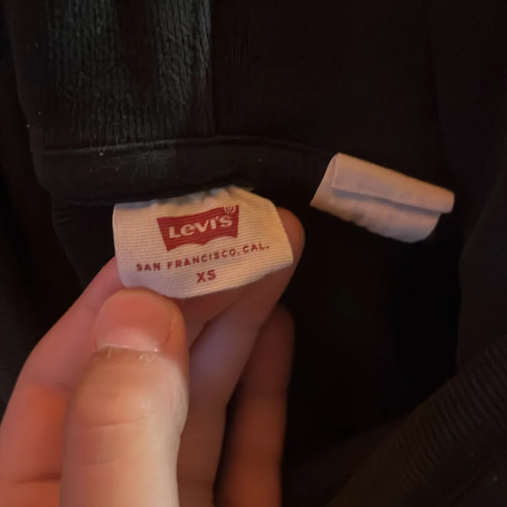 En svart hoodie från Levi's med en liten röd logotyp på bröstet. Hoodien har en justerbar huva med dragsko och långa ärmar.. Tröjor & Koftor.